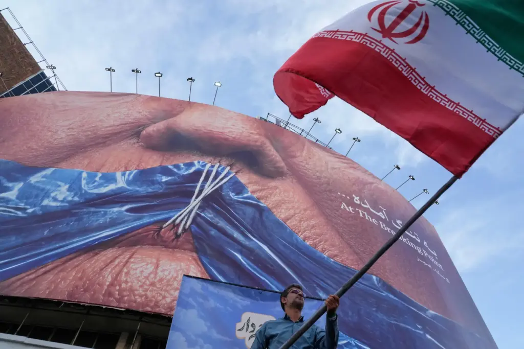 A man waves an Iranian flag in front of a billboard showing Trump's lips shown shut.