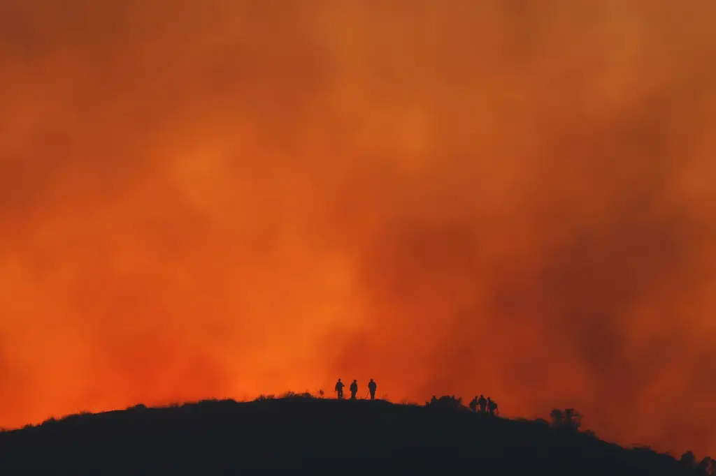 FILE – Firefighters are silhouetted amid an operation to control...