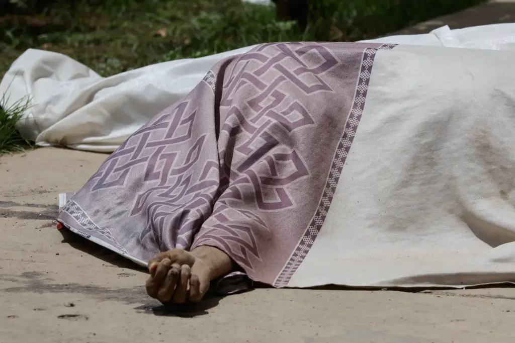 A covered body lies in front of a damaged building...