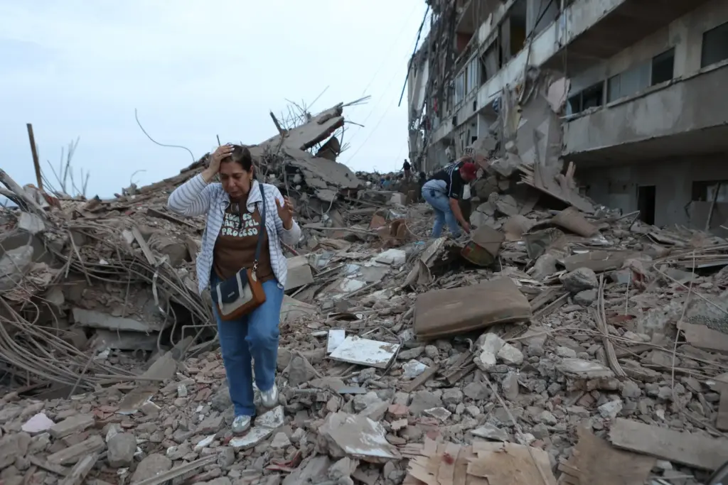 Residents walk among the rubble of building damaged in earthquakes...