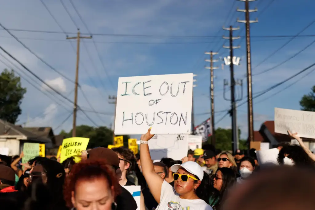 A woman holds a sign reading “ICE OUT OF HOUSTON”...