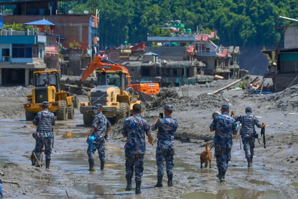 Nepalese policemen watch as earthmovers clear the debris of flash...