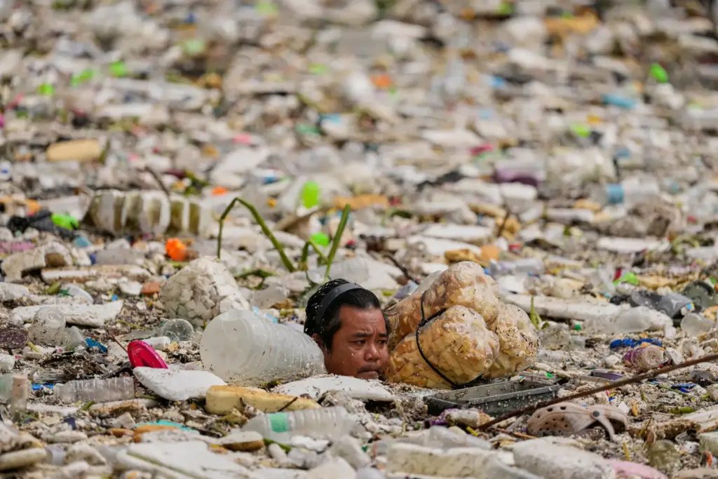 A worker uses improvised floats while trying to clear a sea of garbage.