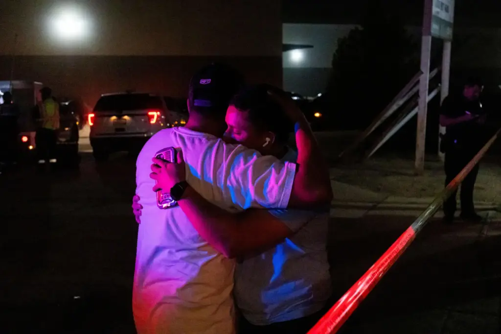 Two people hug each other behind police lines at the scene of a helicopter crash.